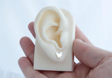 a white prop ear with a handmade sterling silver chicken silhouette stud earring on the ear lobe